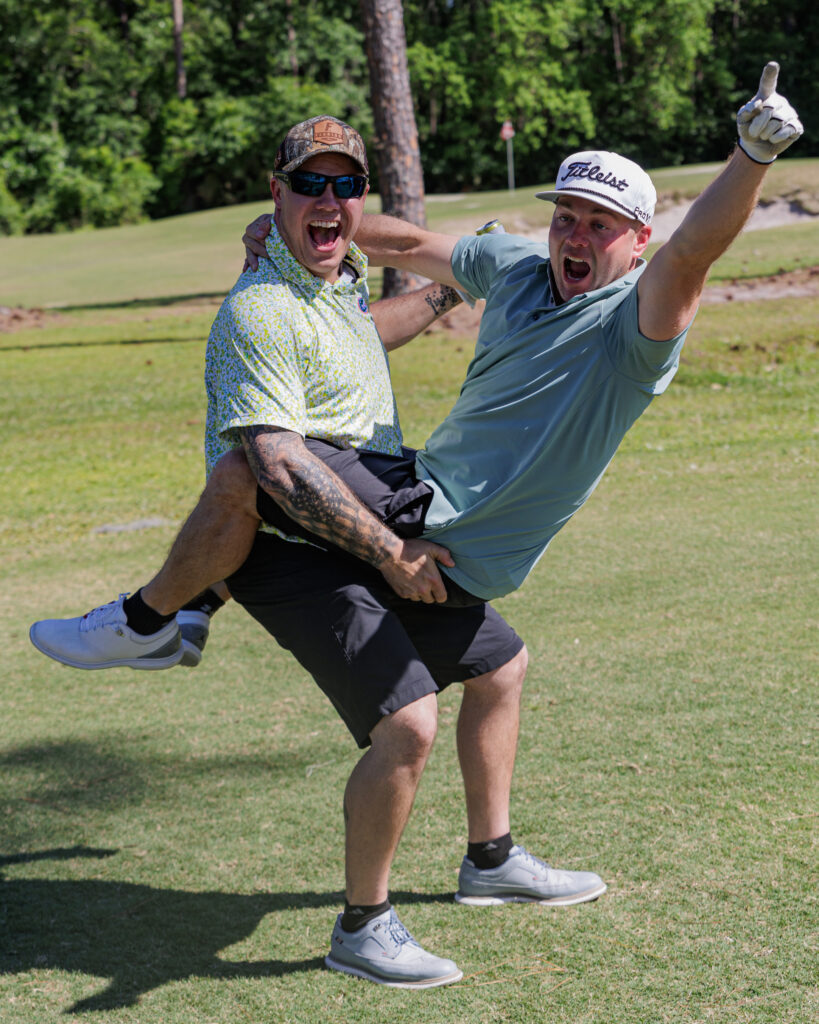 Photo of two golf players from Golf Wars 2024, one man is holding the other in a celebratory pose.