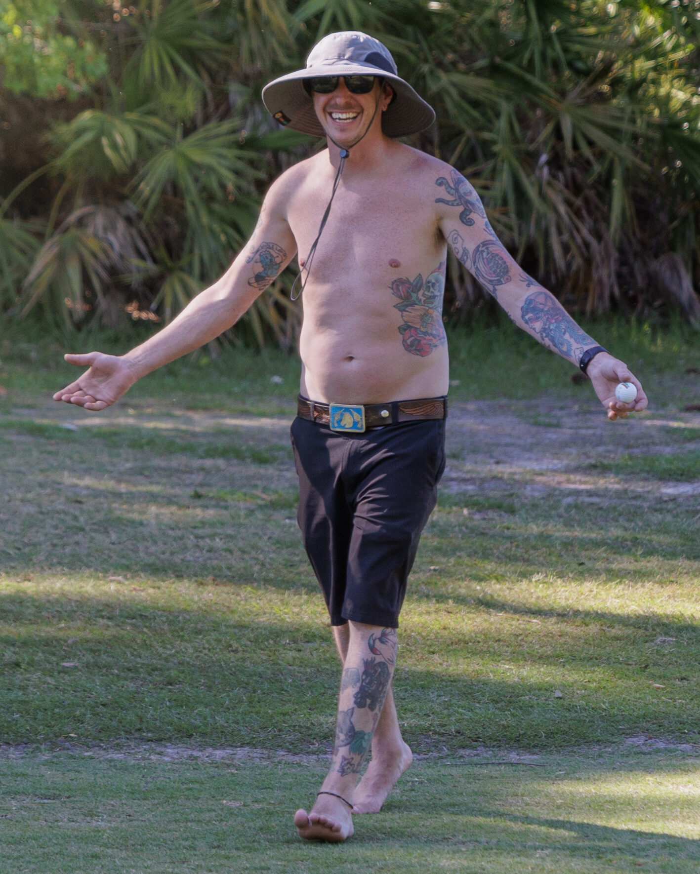 Photo of a shirtless, shoeless man with multiple tattoos, walking on a golf course during Golf Wars 2024.