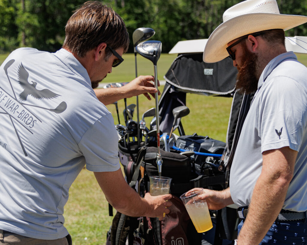 Photo of 2 players from Golf Wars 2024 pouring glasses of beer from a custom keg tap which is fashioned to look like a golf club bag.