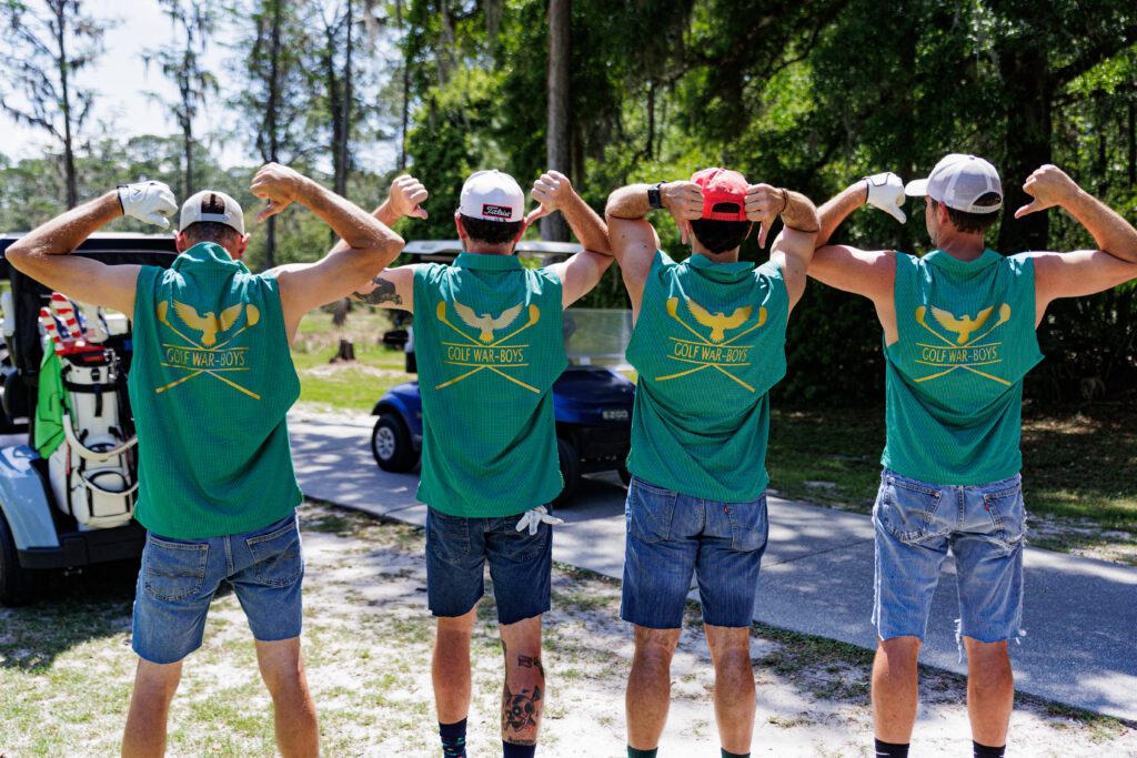 Team Photo from Golf Wars 2025. The team is facing away from the camera, and all 4 members are wearing matching collared shirts which have the words "Golf War-Boys" written on the back of their green shirts.